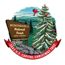 A brown sign next to a pine tree with snow and colorful balls hanging from the branches. The words "Monongalia National Forest West Virginia" are on the brown sign. A red ribbon is below the image with the words "2023 U.S. Capitol Christmas Tree."